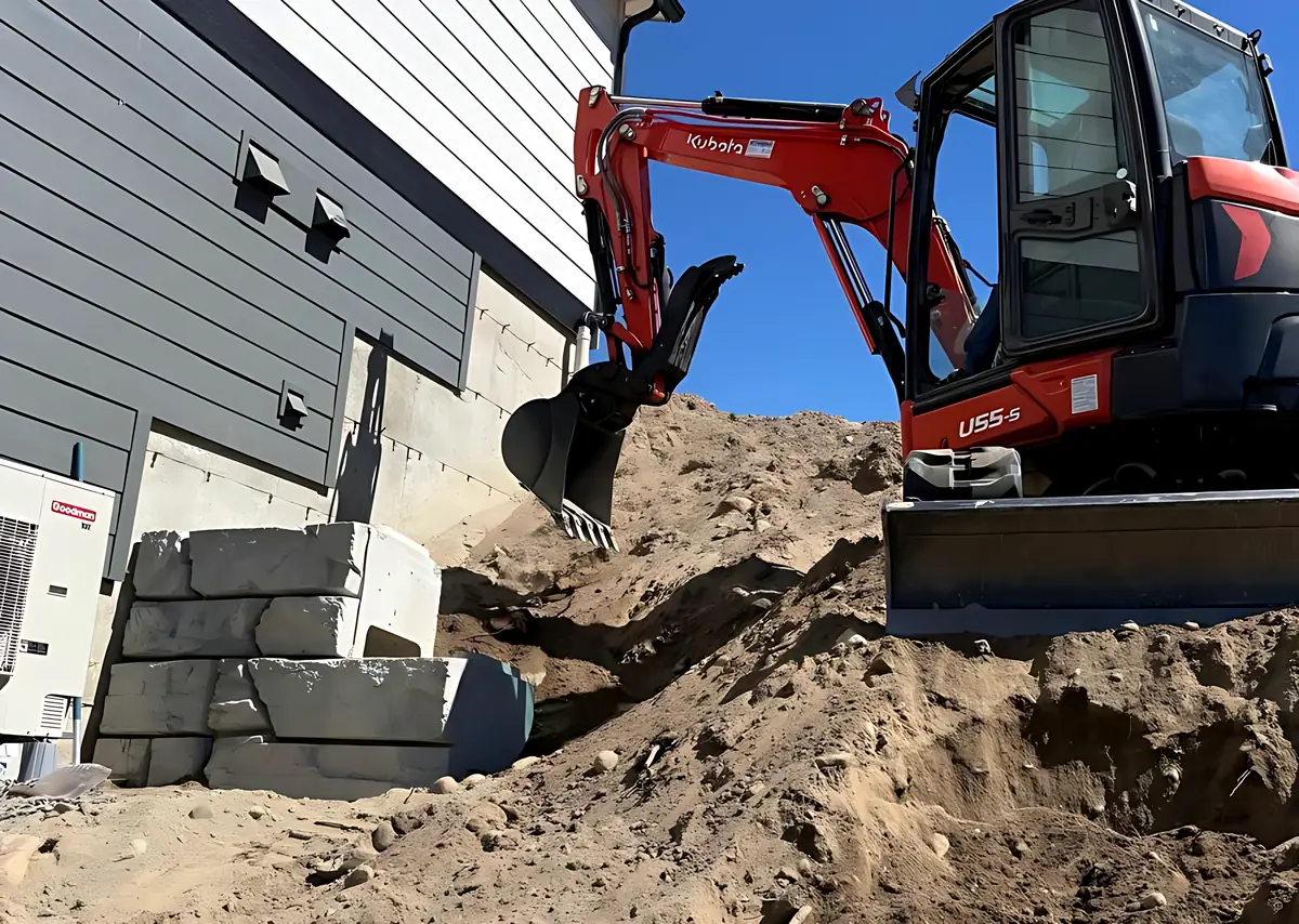 Kubota U55-5 excavator digging beside a house next to a stacked concrete block wall