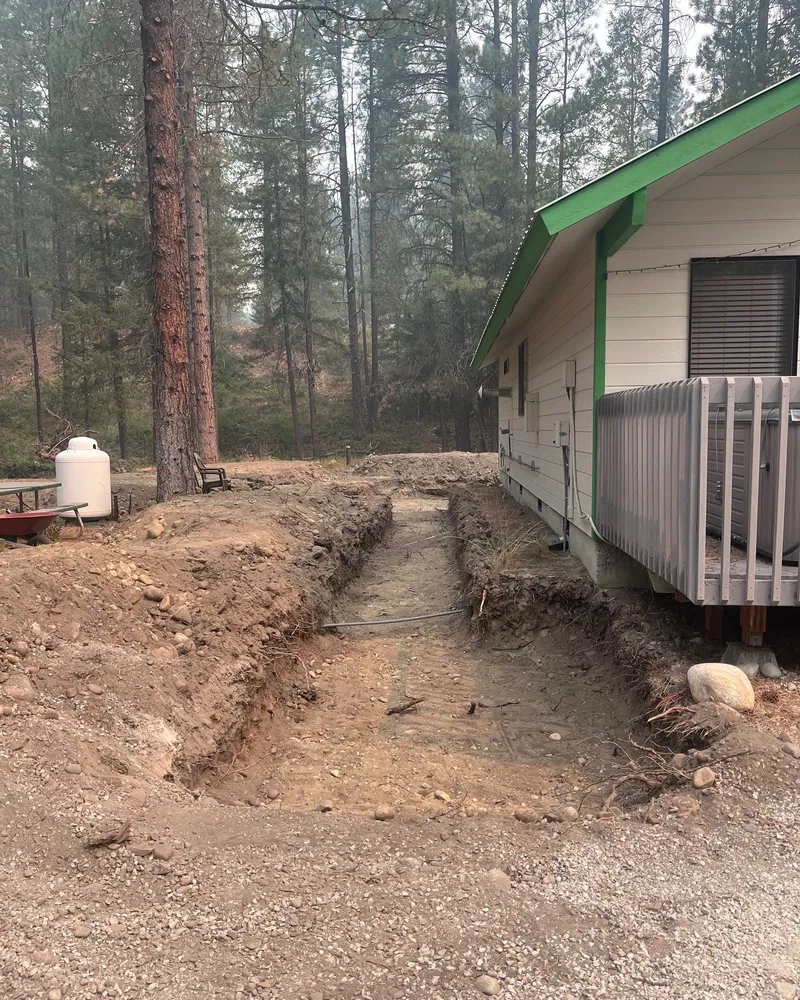Trench cut along the side of the house with pipe in the bottom, propane tank beyond